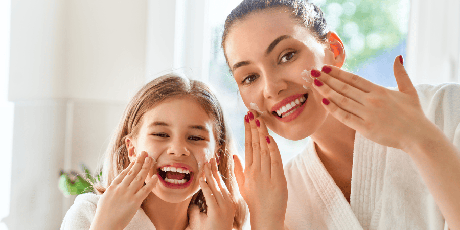 Madre e hija aplicando crema facial juntas, sonriendo