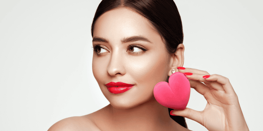 Mujer con maquillaje glow y piel impecable sosteniendo un corazón rosa, perfecta para San Valentín.